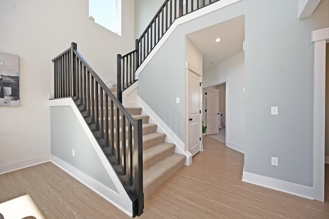 staircase featuring baseboards, wood finished floors, and a towering ceiling