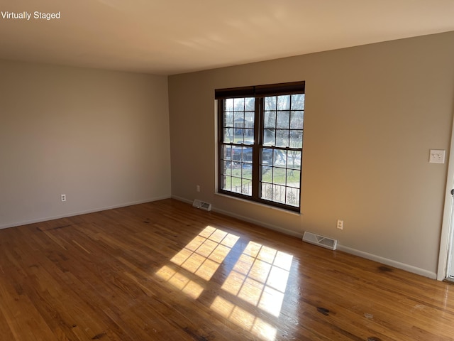 empty room with wood finished floors, visible vents, and baseboards