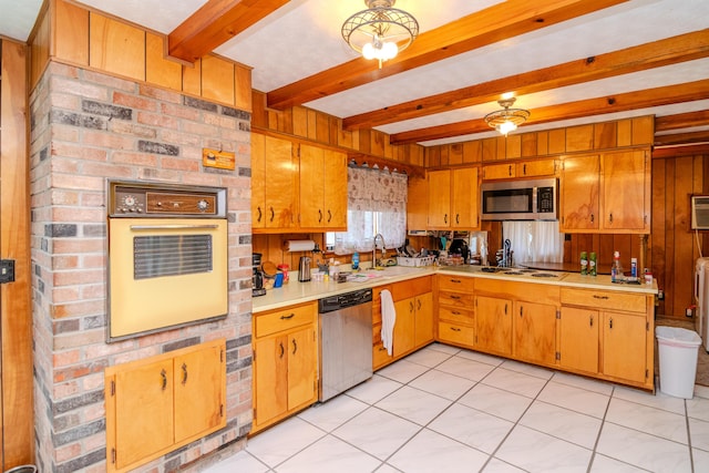 kitchen with beam ceiling, a sink, light countertops, wood walls, and appliances with stainless steel finishes