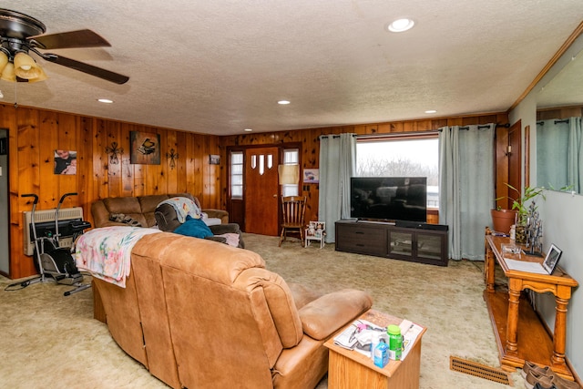 living area with a textured ceiling, recessed lighting, carpet, wooden walls, and ceiling fan