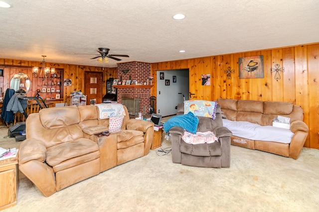 living area with ceiling fan with notable chandelier, carpet flooring, a fireplace, and a textured ceiling