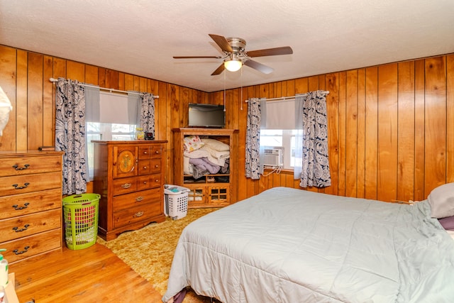 bedroom with a ceiling fan, a textured ceiling, wood finished floors, cooling unit, and wood walls