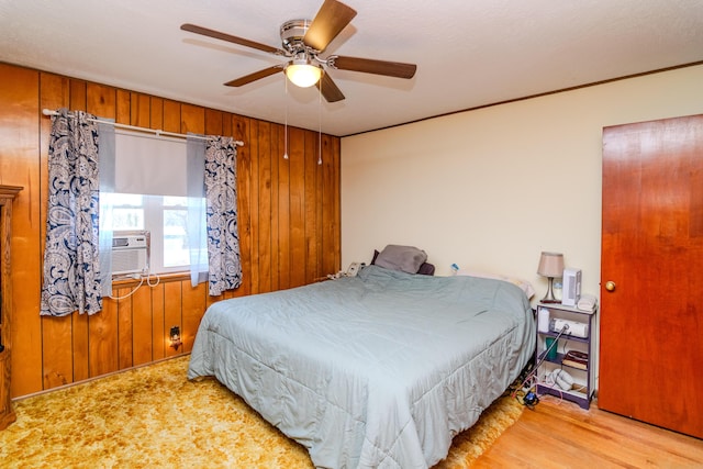bedroom featuring wood walls, cooling unit, a ceiling fan, and wood finished floors