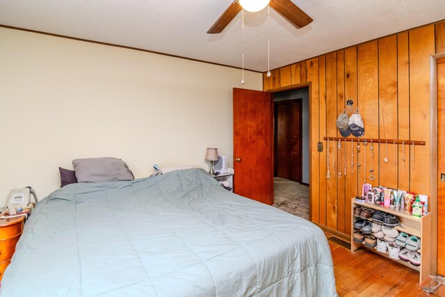 bedroom with wooden walls, ornamental molding, wood finished floors, and ceiling fan