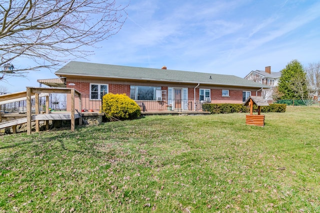 rear view of property featuring brick siding, a lawn, and a deck