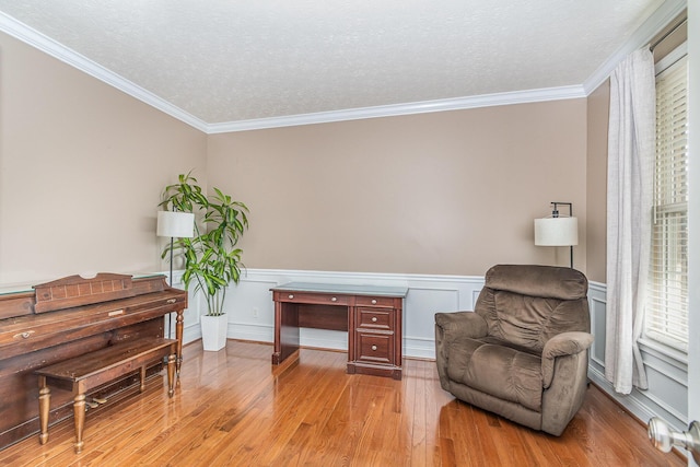 sitting room featuring light wood finished floors, a wainscoted wall, a textured ceiling, and crown molding