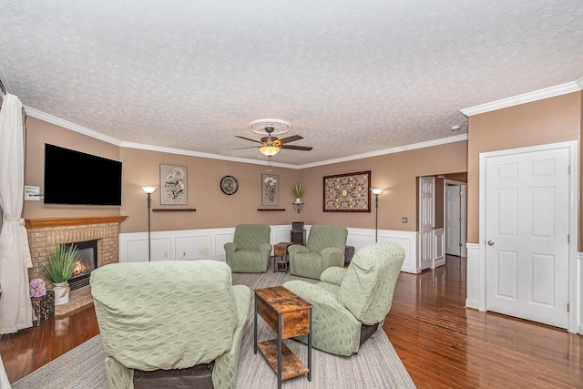 living area featuring a ceiling fan, wood finished floors, a wainscoted wall, and a textured ceiling