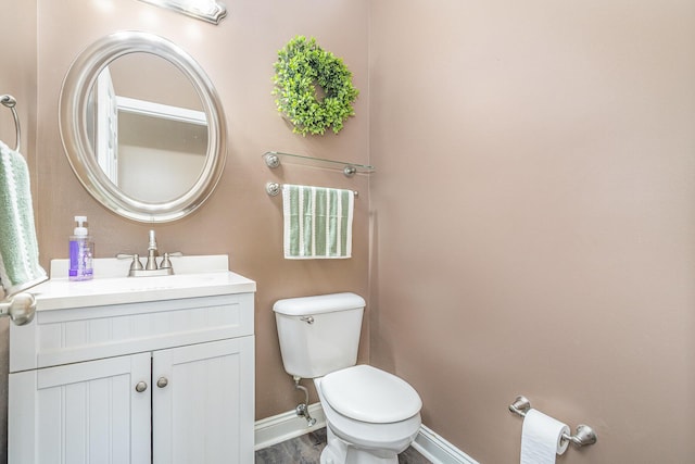 half bath with baseboards, toilet, wood finished floors, and vanity