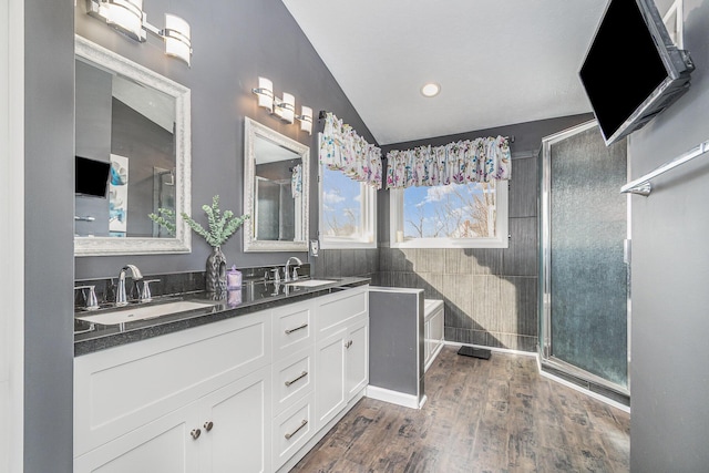 full bath with a shower with door, double vanity, wood finished floors, and a sink