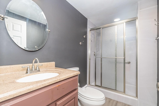 bathroom featuring wood finished floors, toilet, a stall shower, and vanity