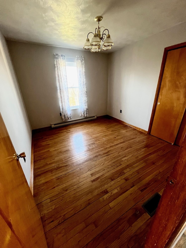 empty room featuring hardwood / wood-style floors, an inviting chandelier, baseboards, and a baseboard radiator