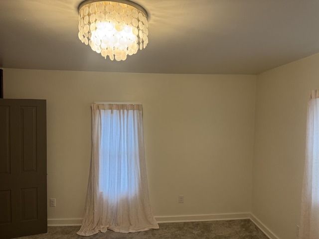 carpeted spare room featuring baseboards and an inviting chandelier