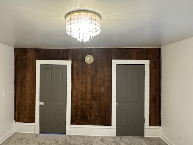 empty room with a notable chandelier, baseboards, carpet floors, and wood walls