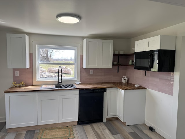 kitchen with a sink, black appliances, white cabinetry, tasteful backsplash, and butcher block counters