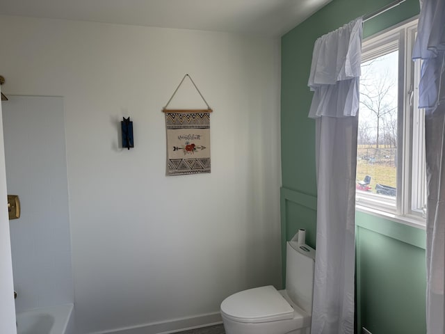 bathroom featuring toilet, bathing tub / shower combination, and baseboards