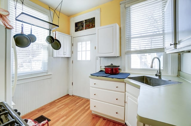 kitchen with visible vents, a sink, light countertops, light wood-style floors, and white cabinetry