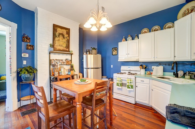 kitchen with freestanding refrigerator, a sink, under cabinet range hood, a notable chandelier, and white gas range