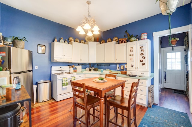 kitchen featuring white gas range, under cabinet range hood, white cabinets, light wood finished floors, and a chandelier