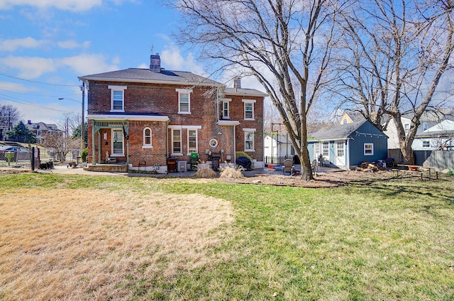 back of house featuring brick siding, a lawn, a chimney, and fence