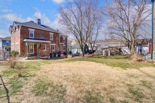 back of house with a yard, fence, brick siding, and a chimney