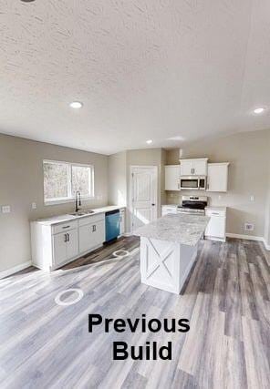 kitchen featuring wood finished floors, appliances with stainless steel finishes, white cabinetry, and a sink