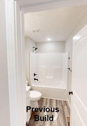 full bath featuring wood finished floors, visible vents,  shower combination, a textured ceiling, and toilet