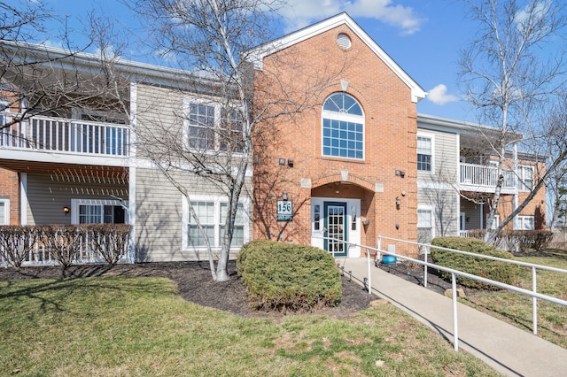 view of front of house with brick siding, a front yard, and a balcony