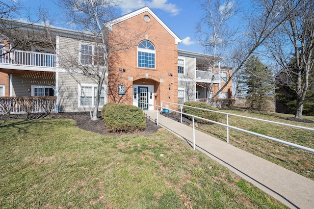 view of front of home with a front yard, brick siding, a balcony, and fence