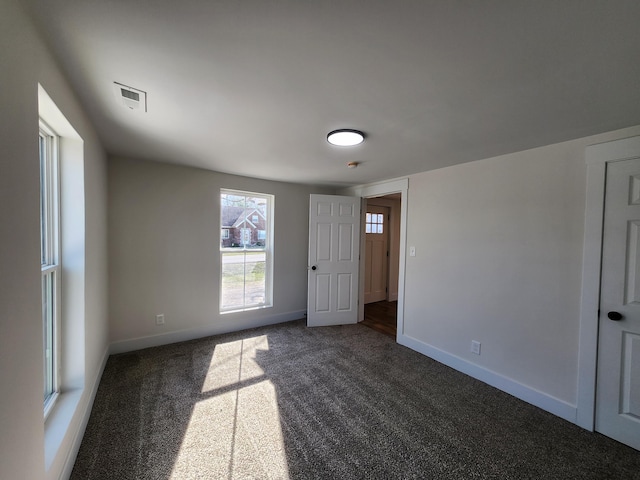 unfurnished room with visible vents, baseboards, and dark carpet