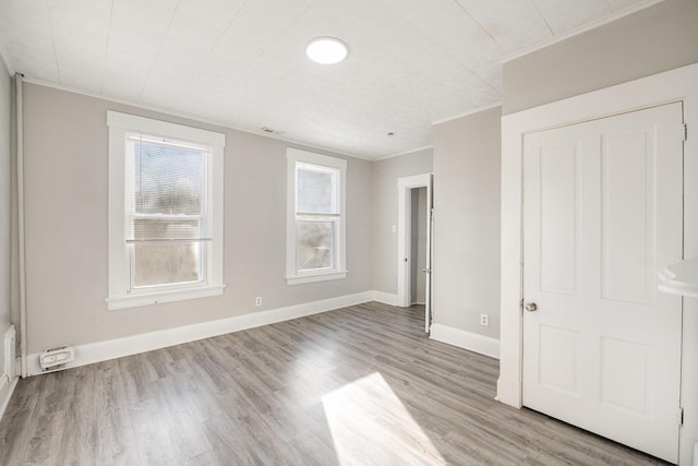 unfurnished bedroom featuring visible vents, baseboards, crown molding, and light wood-style floors