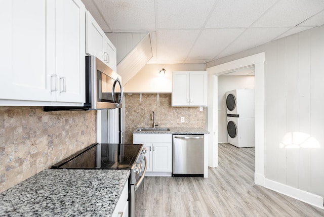 kitchen with light wood-type flooring, stacked washer and dryer, appliances with stainless steel finishes, white cabinets, and a sink