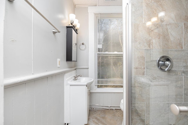 full bath featuring tiled shower, toilet, vanity, and wainscoting