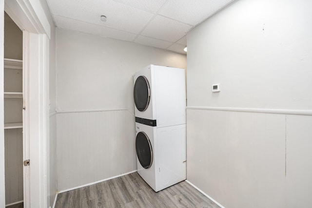 washroom featuring laundry area, stacked washer and dryer, light wood-style flooring, and a wainscoted wall