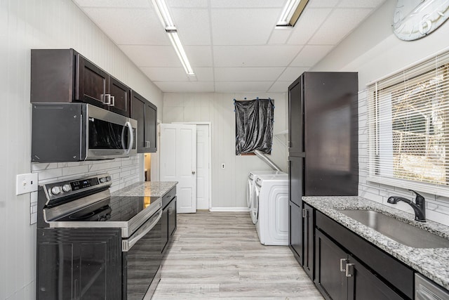 kitchen with light wood finished floors, washer and clothes dryer, a drop ceiling, stainless steel appliances, and a sink