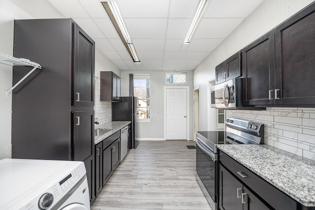 kitchen featuring a sink, washer / clothes dryer, stainless steel appliances, light wood finished floors, and decorative backsplash