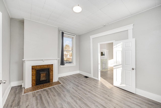 unfurnished living room with visible vents, baseboards, wood finished floors, and a tiled fireplace