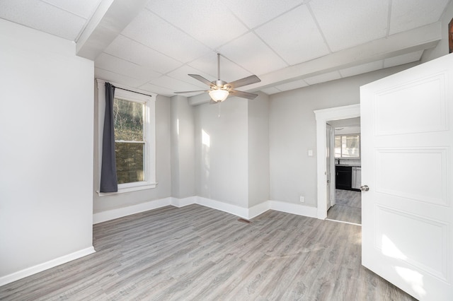 unfurnished room featuring light wood-type flooring, a drop ceiling, baseboards, and ceiling fan