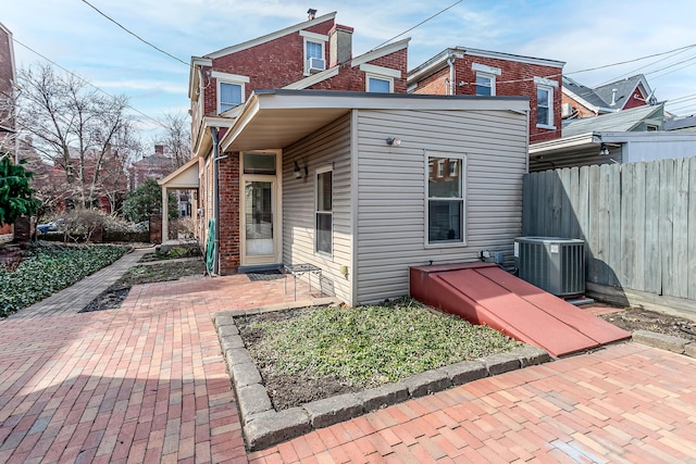 rear view of house with brick siding, a patio, central AC, and fence