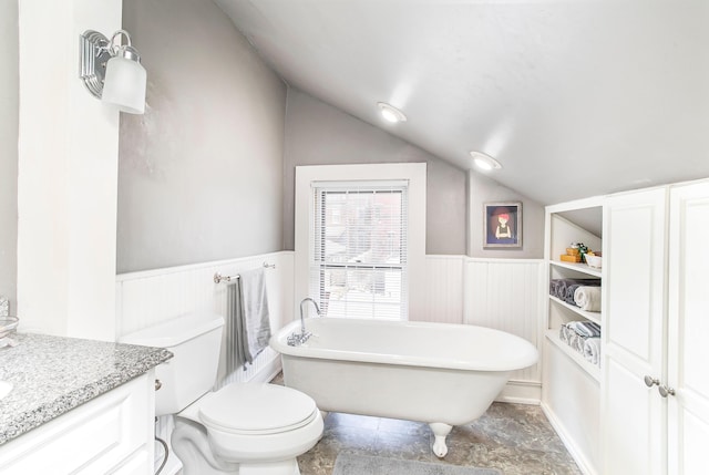 bathroom featuring vanity, a wainscoted wall, a soaking tub, vaulted ceiling, and toilet