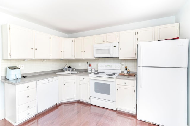 kitchen with backsplash, light countertops, light wood-style floors, white appliances, and a sink