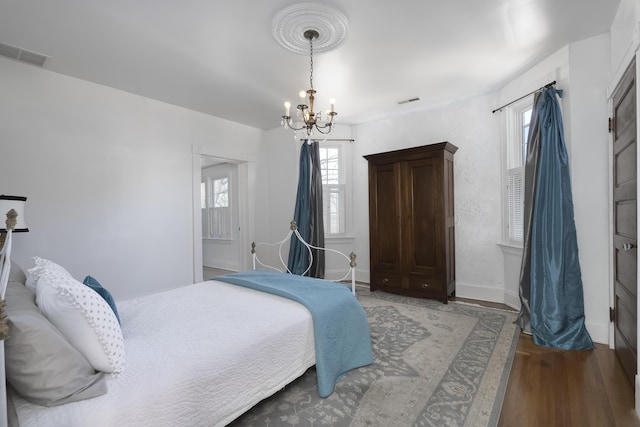 bedroom featuring a notable chandelier, visible vents, baseboards, and wood finished floors