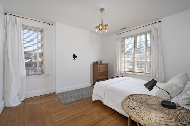 bedroom featuring visible vents, baseboards, a notable chandelier, and wood finished floors