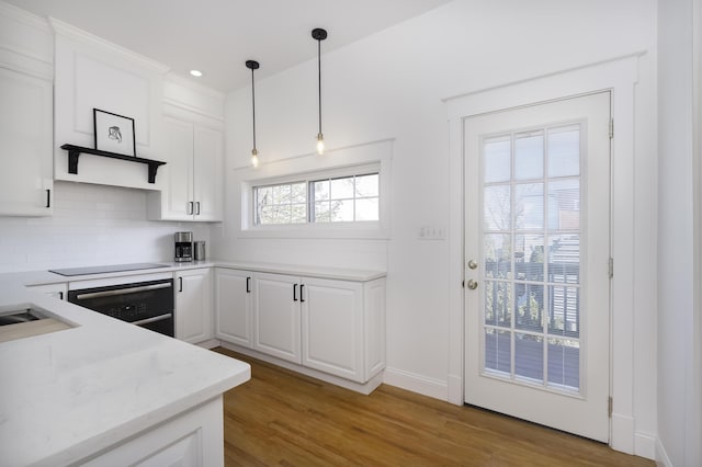 kitchen with backsplash, wall oven, light wood-type flooring, white cabinetry, and black electric cooktop