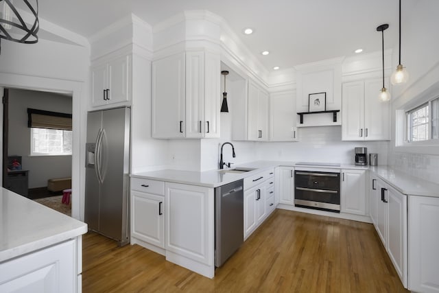 kitchen with a sink, stainless steel appliances, white cabinets, light wood-type flooring, and backsplash