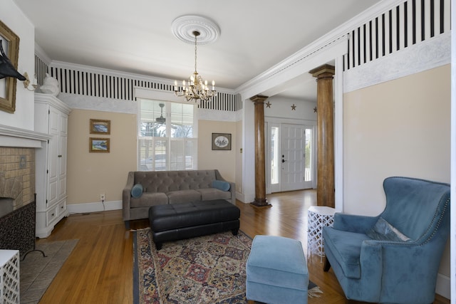 living room featuring a chandelier, baseboards, ornate columns, and wood finished floors