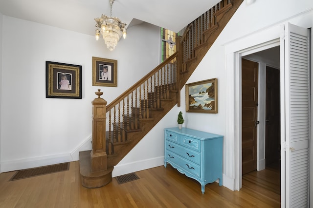 stairway with a chandelier, visible vents, baseboards, and wood finished floors