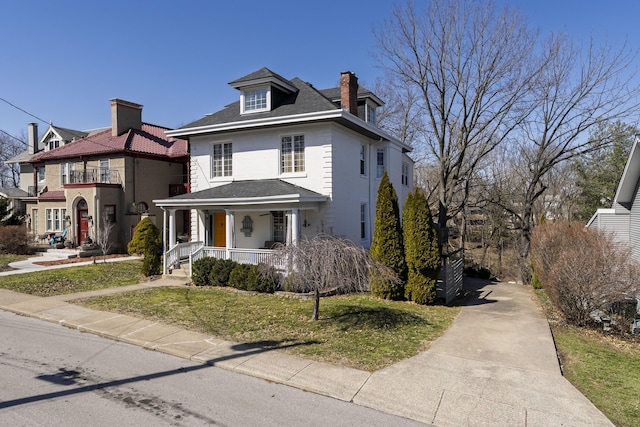 american foursquare style home with covered porch, a chimney, and a front lawn