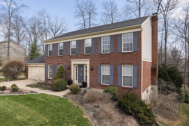 colonial home with driveway, a front yard, a garage, brick siding, and a chimney