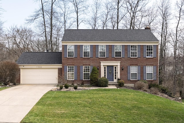 colonial house featuring driveway, a front yard, an attached garage, brick siding, and a chimney