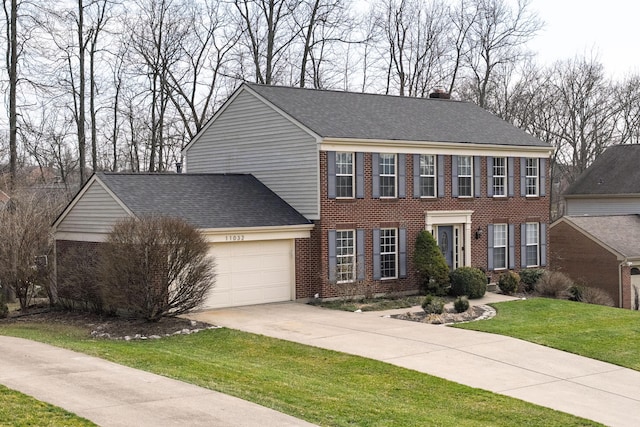 colonial inspired home with brick siding, an attached garage, driveway, and a front yard